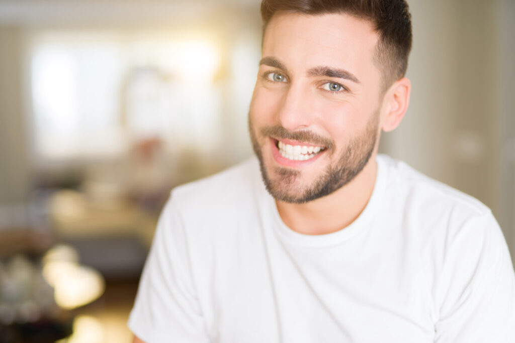 handsome man wearing casual white t-shirt at home looking away to side with smile on face