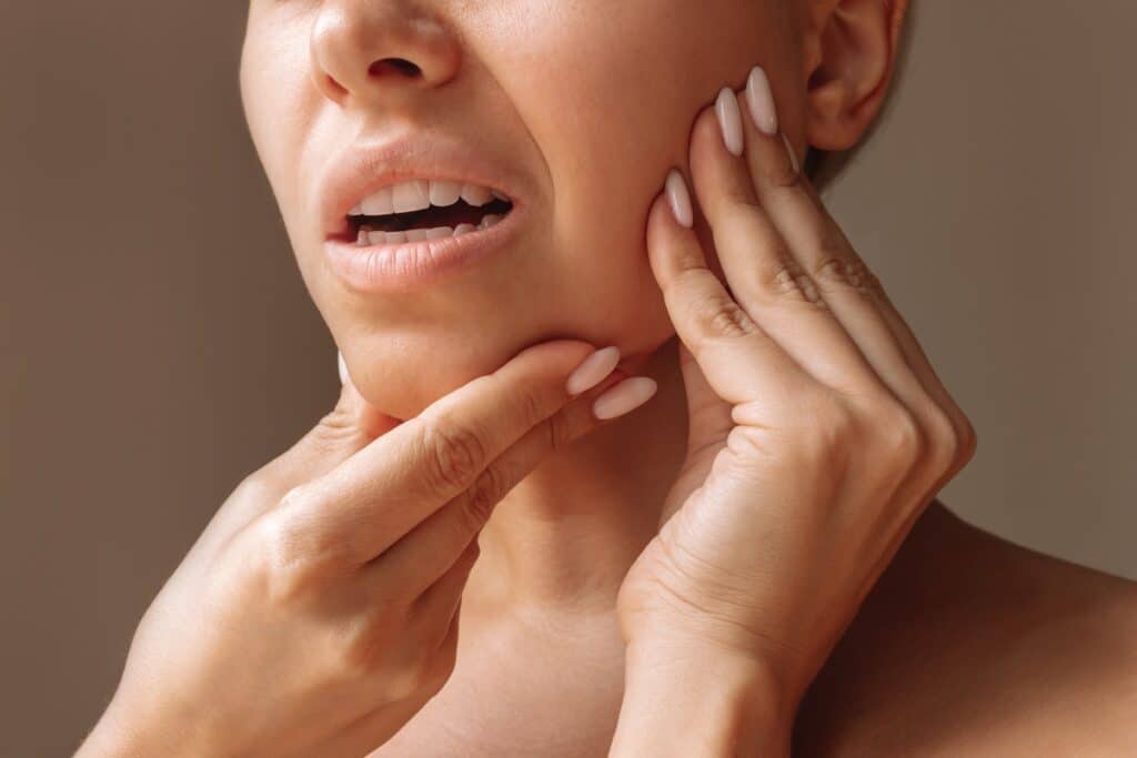 A woman with jaw pain holding her chin and cheek