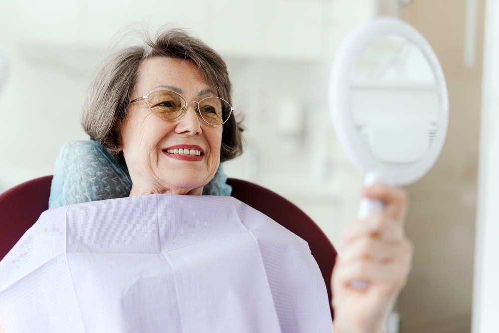 A woman looking in the mirror after teeth cleaning in Spokane