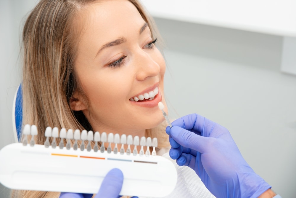 A dentist holding up porcelain veneer shade samples to a patient’s teeth